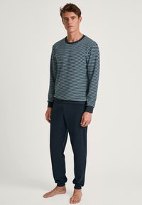 Marine gestreepte longsleeve top met geribbelde manchetten, gecombineerd met effen marineblauwe tapered broeken. Zachte stof, relaxed fit en enkelmanchetten.