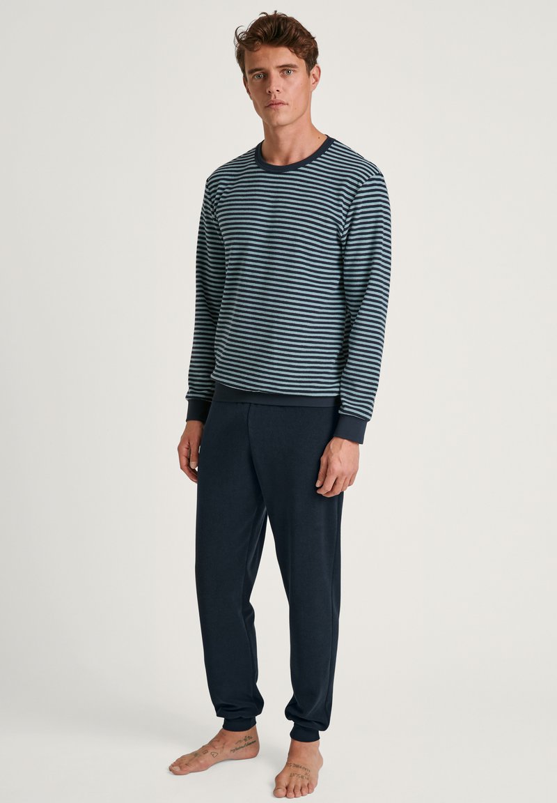 Marine gestreepte longsleeve top met geribbelde manchetten, gecombineerd met effen marineblauwe tapered broeken. Zachte stof, relaxed fit en enkelmanchetten.
