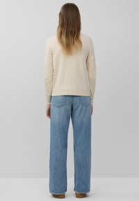 Beige gebreide trui met een ronde halslijn, gecombineerd met lichtblauwe denim jeans met een brede pijp en achterzakken. Zachte textuur, casual pasvorm.