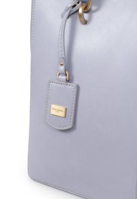 Borsa a mano in pelle lilla chiaro con anello in metallo dorato, etichetta con logo impresso e superficie liscia. Design semplice con una forma strutturata.