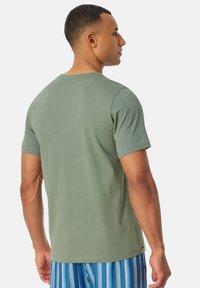 Oliwkowa koszulka z krótkim rękawem z bawełny; okrągły dekolt; gładka faktura; noszona z niebieskimi spodniami w paski.