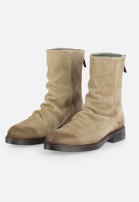 Botas de tobillo de ante en un tono beige claro con un diseño arrugado, punteras redondas y suelas de goma marrón; presentan pequeñas lengüetas en la parte trasera.