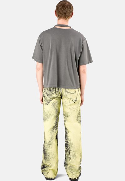 Gray t-shirt with a relaxed fit and crew neck; paired with yellow jeans featuring a black graphic pattern and wide-leg silhouette.