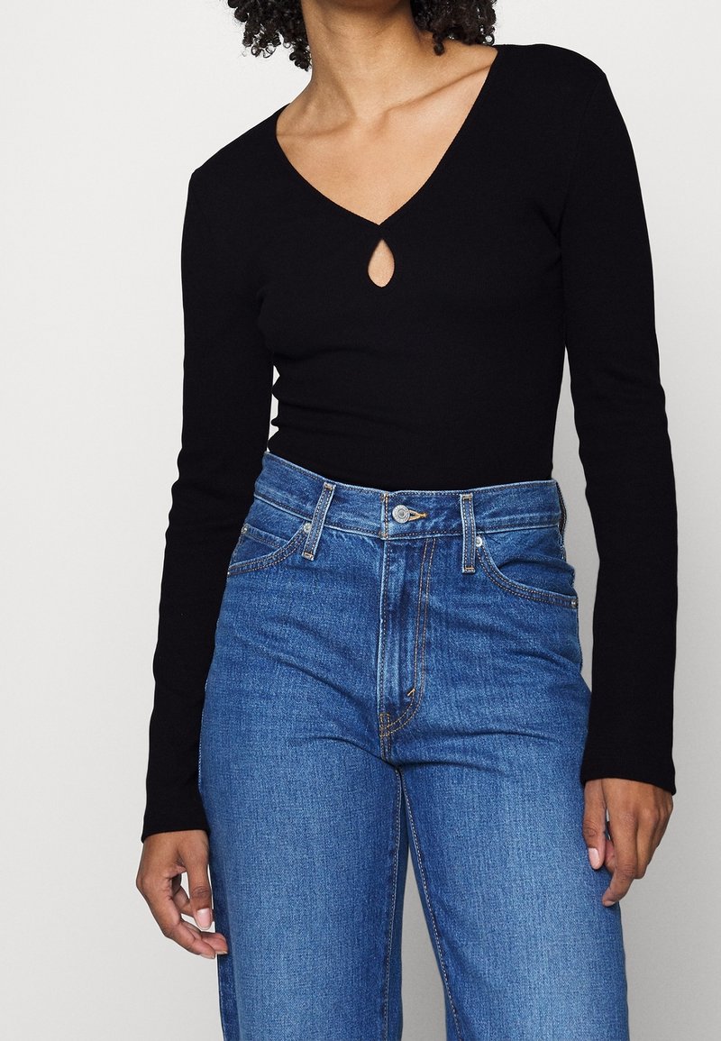 Schwarzer Langarmbodysuit mit tiefem V-Ausschnitt und Schlüssellochdetail, kombiniert mit hochtaillierten blauen Denim-Jeans. Glatte Textur, figurbetontes Design.