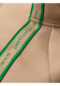 Felpa beige con nastro logo verde ad alte prestazioni. Tessuto liscio con una finitura strutturata, che enfatizza il design moderno e l'estetica sportiva.