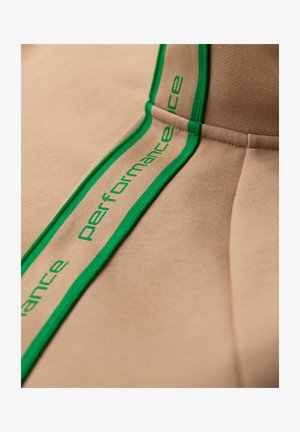Beige Sweatshirt mit grünem Performance-Logo-Band. Glattes Gewebe mit strukturierter Oberfläche, das modernes Design und sportliche Ästhetik betont.