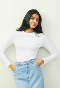 Vit långärmad ribbad topp tillsammans med en ljusblå denimkjol. Kjolen har framfickor och knäppning med knapp.