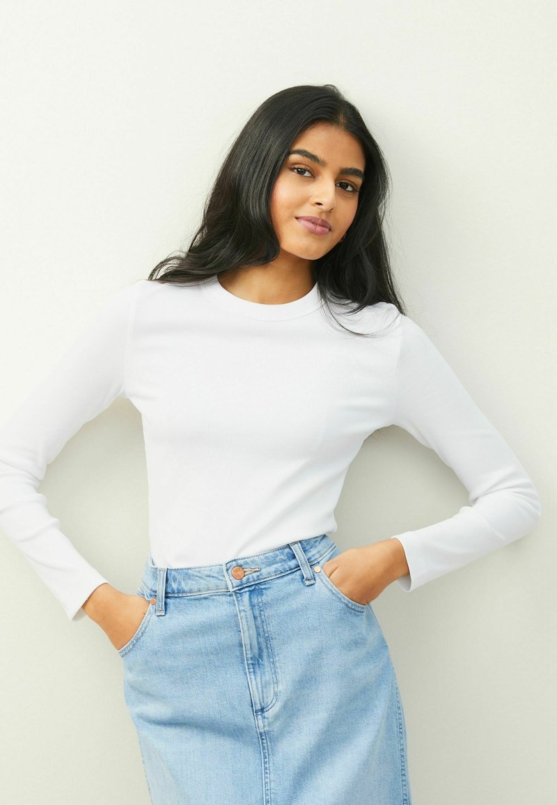 Vit långärmad ribbad topp tillsammans med en ljusblå denimkjol. Kjolen har framfickor och knäppning med knapp.