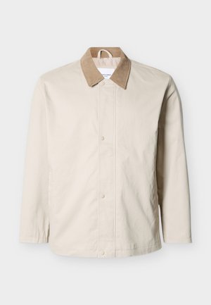 Giacca leggera beige con colletto in velluto a coste color cognac, bottoni a pressione frontali e maniche lunghe su sfondo bianco.