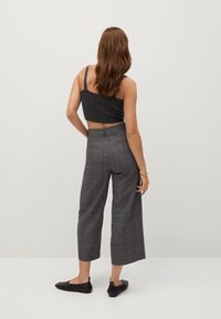 Pantalons à taille haute en plaid gris avec des jambes larges, associés à un crop top sombre et des chaussures plates noires. Texture lisse, motif à carreaux subtil.
