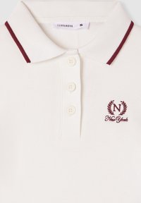 Polo bianco con colletto a righe bordeaux, tre bottoni e logo ricamato "N" accompagnato da alloro e testo "New York". Tessuto testurizzato.