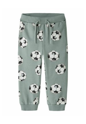Pantaloni della tuta verdi per bambini con motivi di palloni da calcio in bianco e nero, vita elasticizzata, coulisse e polsini alle caviglie.