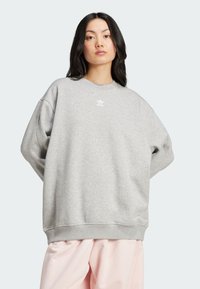 Sweatshirt gris clair en mélange de coton avec épaules tombantes. Il présente un petit logo blanc sur la poitrine ainsi que des poignets et un ourlet côtelés.