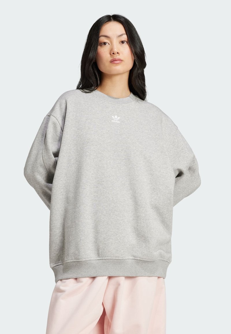 Sweatshirt gris clair en mélange de coton avec épaules tombantes. Il présente un petit logo blanc sur la poitrine ainsi que des poignets et un ourlet côtelés.