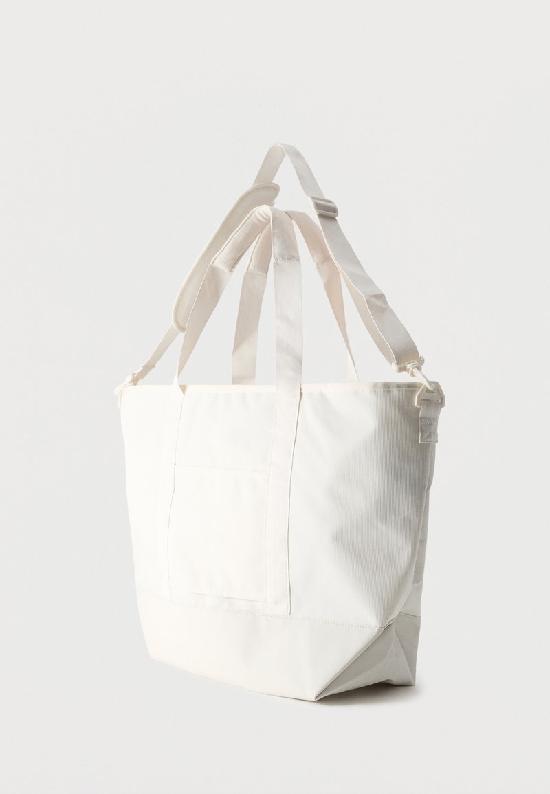 Weiße Canvas-Tragetasche mit doppelten Griffen und verstellbarem Schulterriemen, vor einem schlichten hellen Hintergrund gezeigt.