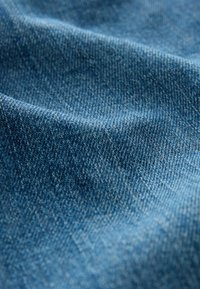 Denim stof met een gestructureerd oppervlak in verschillende tinten blauw, met een klassieke keperweving en lichte vervaging voor diepte.