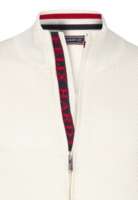 Witte zip-up trui met een gestructureerd patroon, met een rood en marineblauw gestreepte kraag en een gemarkeerde ritssluiting met het merk "FELIX HARDY."