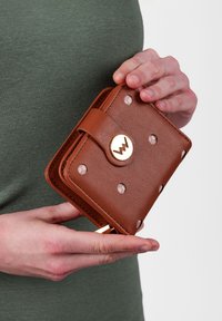 Brown textured wallet with gold hardware, featuring circular cutouts. It has a flap closure and is being held with a hand.