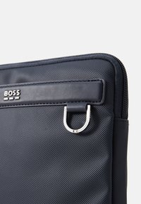 Funda para portátil azul marino hecha de material texturizado, con un lazo de hardware plateado y un acento de cuero negro con la marca BOSS.