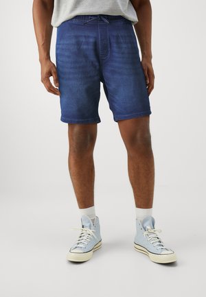 Pantalones cortos de mezclilla azul con cintura elástica y cordones, con un ajuste relajado y corta longitud, combinados con zapatillas de caña alta azul claro.