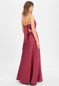 Lange bordeauxrode avondjurk met een geknoopte achterkant, verstelbare spaghetti-bandjes, vloeiende stof en een gladde, satijnen textuur.