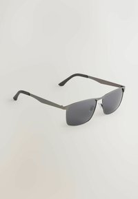 Lunettes de soleil rectangulaires en métal gris avec des verres teintés foncés et des branches incurvées noires sur un fond clair uni.