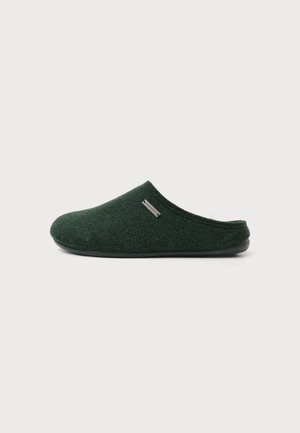 Chausson vert foncé à enfiler, fermé à l’avant, avec une tige en tissu doux et une semelle noire sur un fond clair uni.