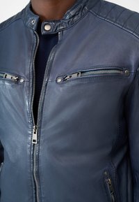 Marineblaue Lederjacke mit Stehkragen, durchgehendem Reißverschluss und dekorativer Naht. Zwei Brusttaschen mit Reißverschluss.
