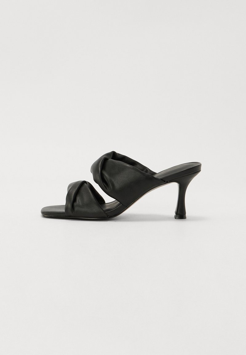 Sandales à talons noirs avec des lanières nouées en douceur, bout ouvert et un talon aiguille élégant. Fabriquées en matériau lisse avec un design minimaliste.
