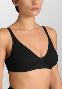 Seno nero wireless con design a V, tessuto morbido, spalline regolabili e senza hardware visibile; la struttura senza cuciture aumenta il comfort.