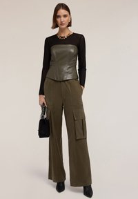 Top de corsé de cuero verde olivo, mangas largas negras transparentes, pantalones cargo anchos de oliva con bolsillos, bolso negro, botines negros con tacón, collar colorido.