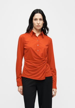 Červená dlouhý rukáv halenka s řasením v pase, zapínáním na knoflíky u límce, hladkou látkou a lesklými knoflíky. Kombinována s černými kalhotami.