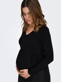 Czarna sukienka ciążowa z długim rękawem, dopasowaną górą i luźno opadającym dołem, podkreślająca zaokrąglony brzuch. Miękki materiał i dekolt w kształcie litery V.