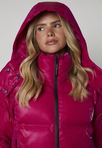 Fuksjowa kurtka puchowa z wysokim kołnierzem i dużym kapturem. Wyposażona w czarny zamek błyskawiczny i napy. Błyszczące wykończenie, pikowana tekstura i boczne kieszenie.