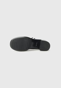 Black shoe sole with horizontal grooves for grip, featuring a rounded shape and smooth edges. Matte finish without visible branding.