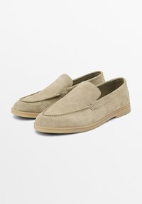 Semišové slip-on boty v světle béžové barvě, s špičatou špičkou a minimálním prošitím. Gumová podrážka v tónu s jemným designovým detailem.