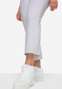 Sneaker alte bianche in pelle testurizzata, con perforazioni e colletto imbottito, abbinate a pantaloni corti grigi chiari con orli grezzi.