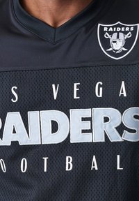 Maglia da football in rete nera con la scritta "LAS VEGAS RAIDERS" in lettere bianche e grigie chiare, e il logo dei Raiders in alto a sinistra.