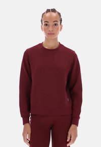Burgundowy sweatshirt z okrągłym dekoltem, wykonany z miękkiego materiału, z długimi rękawami, luźnym krojem, ściągaczami oraz małym akcentem logo.