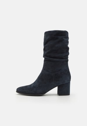 Marineblauwe suède enkelboot met een slouchy ontwerp, puntige neus en een chunky hak. Gladde textuur met minimale stikdetails.