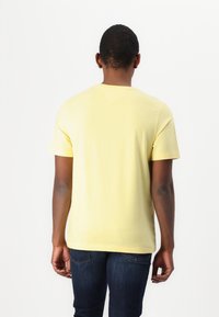 Kortærmet gul t-shirt lavet af blødt stof. Har en rund hals og en glat tekstur. Bæres med mørkeblå jeans.