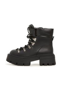 Botines negros con un acabado de cuero brillante, cuello acolchado, suela gruesa tipo lug, ojales de metal y cordones para un detalle estructural.