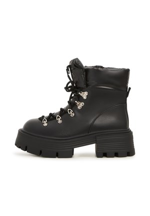 Botines negros con un acabado de cuero brillante, cuello acolchado, suela gruesa tipo lug, ojales de metal y cordones para un detalle estructural.