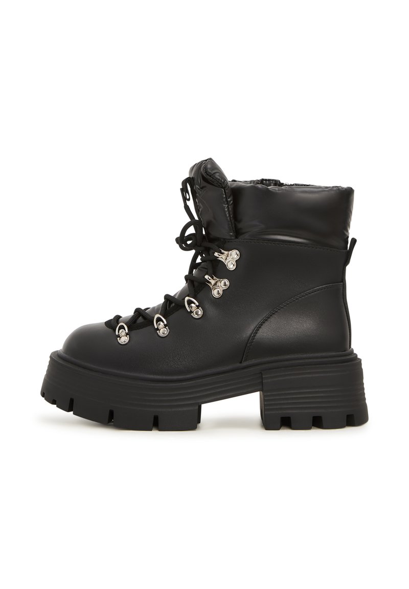 Botines negros con un acabado de cuero brillante, cuello acolchado, suela gruesa tipo lug, ojales de metal y cordones para un detalle estructural.