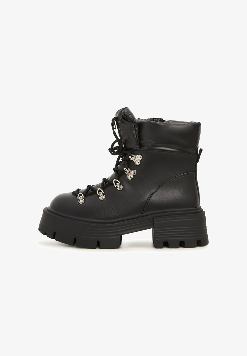 Botines negros con un acabado de cuero brillante, cuello acolchado, suela gruesa tipo lug, ojales de metal y cordones para un detalle estructural.