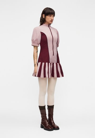 Μπορντό και ανοιχτό ροζ φόρεμα με φερμουάρ μπροστά, φουσκωτά μανίκια και ριγωτή φαρδιά στρίφωση. Φορεμένο με καφέ μπότες μέχρι το γόνατο και καλσόν.