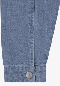 Ljusblå denimtyg med en strukturerad yta, med en knappstängning och sydda detaljer vid ärmslutet.