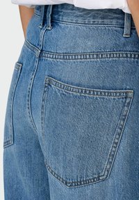 Jeans din denim bleu deschis, cu talie înaltă, două buzunare la spate și detalii de cusătură vizibile, prezentând un design clasic cu cinci buzunare.