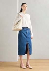 Jeans midi krilo z odprtino spredaj, v kombinaciji s svetlo rebrastim bluzom in bež petami. Belo ročno torbico dopolnjuje obleko.