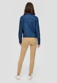 Jeansknappskjorta i mörkblått, med långa ärmar och krage, ihop med slim-fit beige byxor och vita sneakers.